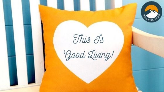 Orange pillow with white heart and cursive "This Is Good Living" written in blue ink on the heart